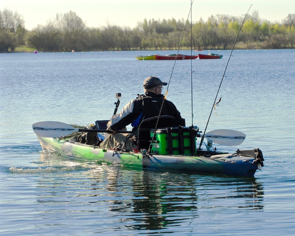 man with multiple rods fishing from an inflatable kayak on a large lake