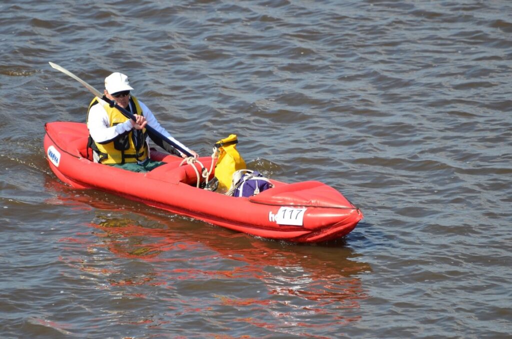 red inflatable kayak on the open water with elderly man paddling